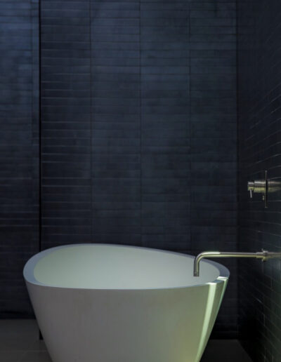 Modern freestanding bathtub in a bathroom with dark tile walls and natural light.