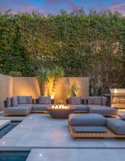 Modern outdoor patio with a fire pit, comfortable seating, and landscape lighting at dusk.