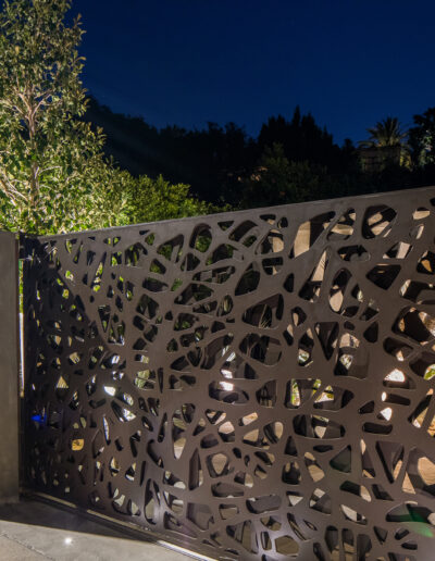 Decorative cut-out fence illuminated at night with trees and a clear sky in the background.