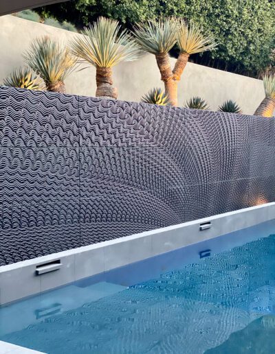 A swimming pool with a decorative textured wall and palm trees in the background.