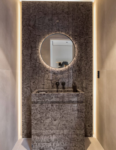 Modern bathroom with a round mirror and stone-textured sink cabinet.