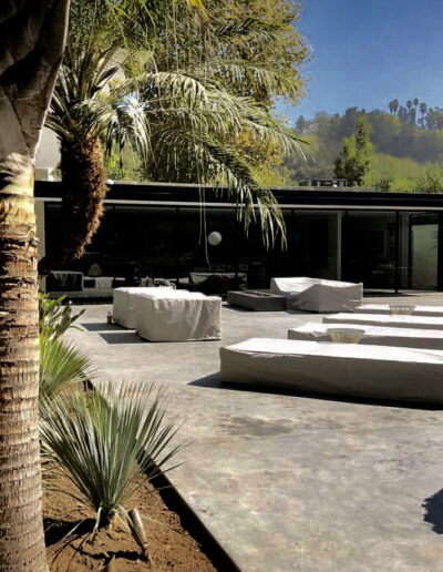 Modern backyard with a pool, concrete patio, and outdoor seating surrounded by lush greenery.