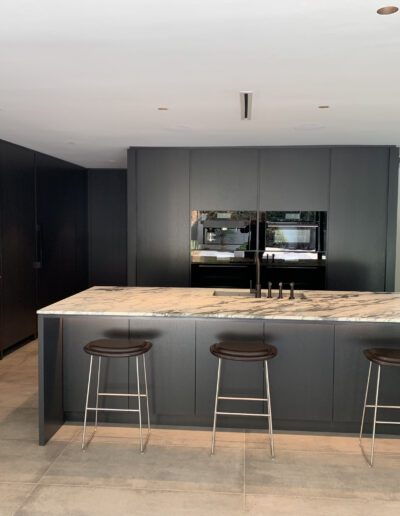 Modern kitchen with black cabinetry, a marble island, and bar stools.